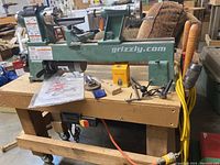 Full view of lathe and custom wooden stand with accessories on top and extension cords hanging.