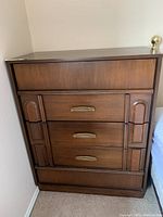 Front view of five-drawer dresser showing decorative carvings and brass-tone handles