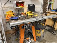 Overview of RIDGID table saw with aluminum fence, cast iron top on stand, attached Shop-Vac and assorted accessories on table surface