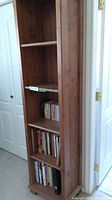 Front view of tall pine wood shelf unit with four shelves, partially filled with books, showing wood grain and overall condition.