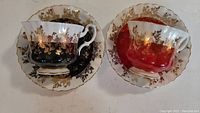 Top-down view of both Royal Albert teacups with matching saucers, one set red and one set black with gold floral details and gilded rims.