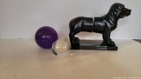 Side view of black dog bookends with purple spherical paperweight and clear coin paperweight positioned on a flat surface.