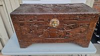 Front view showing carved harbor scene with boats, figures, and detailed floral border with central metal lock