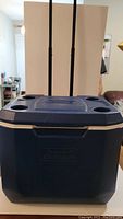Front view of dark blue Coleman rolling cooler with cup holders on lid and dual telescoping handle extended.