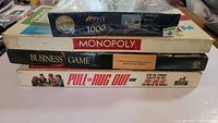 Stack of games including a 1000-piece Perfalock puzzle, Monopoly, Business Game, and Pull the Rug Out game.
