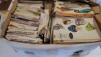 Top-down view into the box filled with vintage sewing pattern envelopes from brands Butterick, McCall's, and Vogue, showing illustrated garments on front.