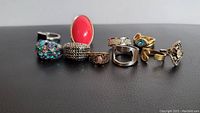 Photo showing seven assorted rings lined up on a black surface highlighting various colors and designs.