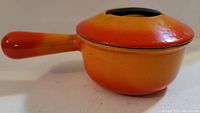 Side view of the small cast iron pot showing the handle and pot shape with gradient orange-yellow enamel coating.