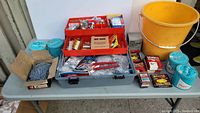 Large assortment of tools and hardware laid out on a table including containers, nails and organized parts.
