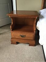 First wooden side table with drawer and open shelf, showing ornate metal handle and curved side supports.