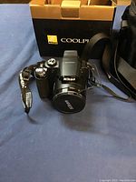 Nikon Coolpix digital camera with lens cover and strap in front of original box