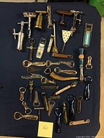 Overview of the collection laid out on a dark blue surface, showing varied types of bottle openers and corkscrews with different handles and styles.