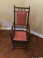 Front view of antique wooden rocking chair showing red upholstered seat and backrest, turned spindle design in wood.