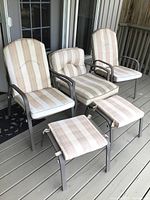 Three cushioned outdoor chairs with metal frames and two matching footstools with striped cushions on a deck.