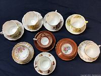 Top-down view of all 9 china tea cups and matching saucers arranged in two rows showing floral patterns and colors