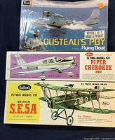 Photo showing three airplane model kit boxes stacked, two sealed in plastic wrapping, one open.