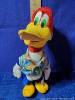 Front view of Woody Woodpecker plush showing colorful shirt and facial details with wooden ruler for size reference.