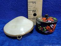 Two trinket keepsake boxes side by side, one oyster shell shaped and one small round hand-painted wooden box with floral designs.