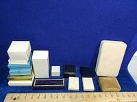 Photo of various jewelry boxes arranged on a blue cloth background showing their sizes against a ruler for scale.