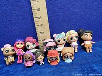 Photo showing 11 small collectible dolls including LOL Surprise and Barbie figures arranged in a line with ruler for size reference, figures 1 to 3 inches tall.