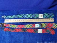 Three new Scottish tartan wool dress ties laid out with a ruler to show length, with distinct patterns of red, blue, green, and yellow in traditional tartan.
