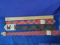 Three wool dress ties laid out with a ruler showing length, all new with tags, tartan and striped patterns visible.