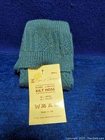 Close-up photo of folded blue knitted kilt hose socks with a yellow tag showing brand, size, material and care instructions.