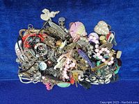 Pile of assorted jewelry items on blue fabric background including necklaces, brooches, chains, and beads