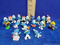 Photo of 13 vintage Schleich Peyo Smurf figures arranged in front of a blue background with a ruler measuring about 5 inches tall to show scale.
