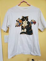 Full front view of vintage white t-shirt with black and white cat appliqued at center chest, surrounded by colorful flowers.