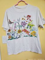 Front view of white vintage t-shirt with colorful print of flowers, butterflies and a hummingbird, showing overall design and condition.