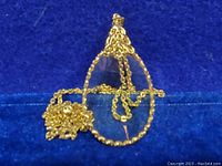 Close-up photo showing the pendant with its gold tone ornate metal frame and magnifier lens, and part of the chain coiled beside it on a dark blue background.