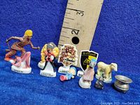 Full lot of mixed vintage miniatures including character figures, house crests, sheep, and small silver objects shown with ruler for scale