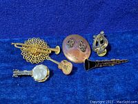 Seven vintage music-themed pins and brooches on blue background, showing variety of instruments and symbols.