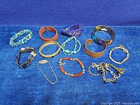 Lot overview showing 11 vintage bracelets including beaded, metal cuff, painted bangle, and charm bracelets arranged on blue cloth.