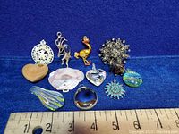 Lot of 11 assorted vintage pendants arranged on blue felt with ruler for size reference.