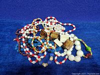 Lot of mixed vintage strung bead necklaces on blue background showing varied bead sizes, colors, and materials including white, red, amber, blue, and pearl-like beads.