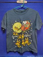 Front view of navy blue vintage Christmas T-shirt showing colorful Snoopy Santa riding sleigh with reindeer in front of a moon and snowflakes.