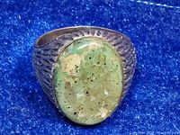 Top and angled top view of the ring showing the large oval green natural stone with mottled pattern and textured sterling silver band and bezel.