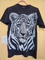 Full front view of the black short-sleeve T-shirt featuring a detailed white tiger face with blue eyes printed on the front.