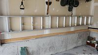 Full length of aluminum extension ladder extended and hung horizontally on garage wall