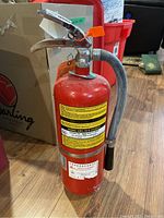 Front side view of red Flag fire extinguisher model ABC-10-G showing instruction label and flexible hose with black nozzle tip.
