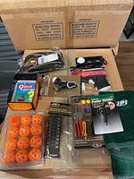 Photo showing Golf accessories including Senators head cover, golf brushes, orange practice balls in tray, golf books and tools spread on a cardboard box.
