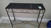 Front angle view of the metal hall table showing black top and decorative metal scrollwork on the apron.