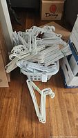 Pile of white plastic clothes hangers bundled and loosely placed on the floor with some wooden hangers inside a laundry hamper.