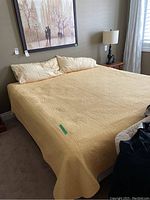 King size bed made with yellow quilted bedspread and pillows, wooden nightstand with lamp beside it.