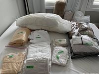 King size bedding items including pillow, several sheets, and pillow shams arranged on a bed, some items sealed in plastic bags.