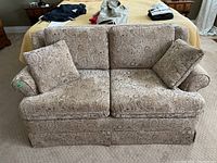 Front view of beige patterned upholstered love seat with two cushions on a carpeted floor.