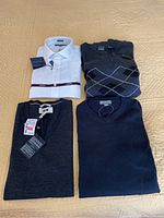 Four men's clothing items laid out on bedding including white Tommy Hilfiger dress shirt and three sweaters.