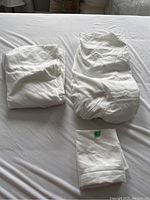 Three white bedding pieces laid out on a bed: fitted sheet, duvet cover, and pillow shams.